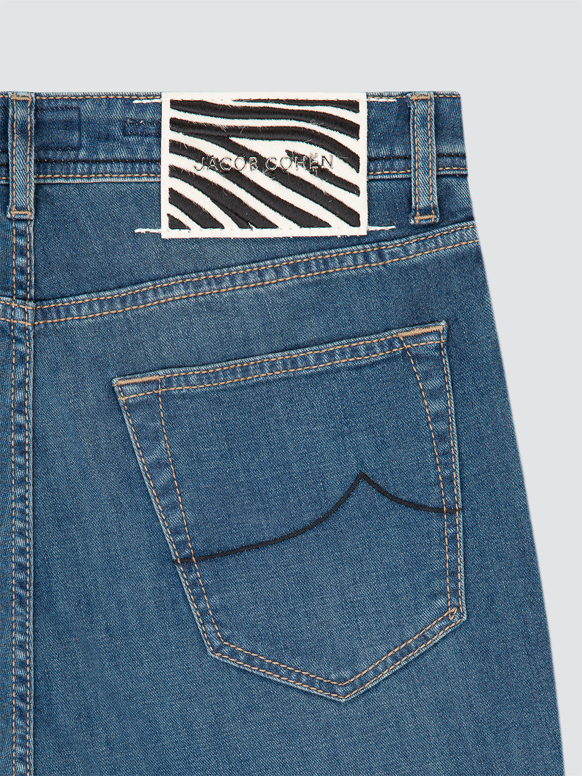 Blue denim jeans with a brand label Jacob Cohen on the back pocket against a light gray background