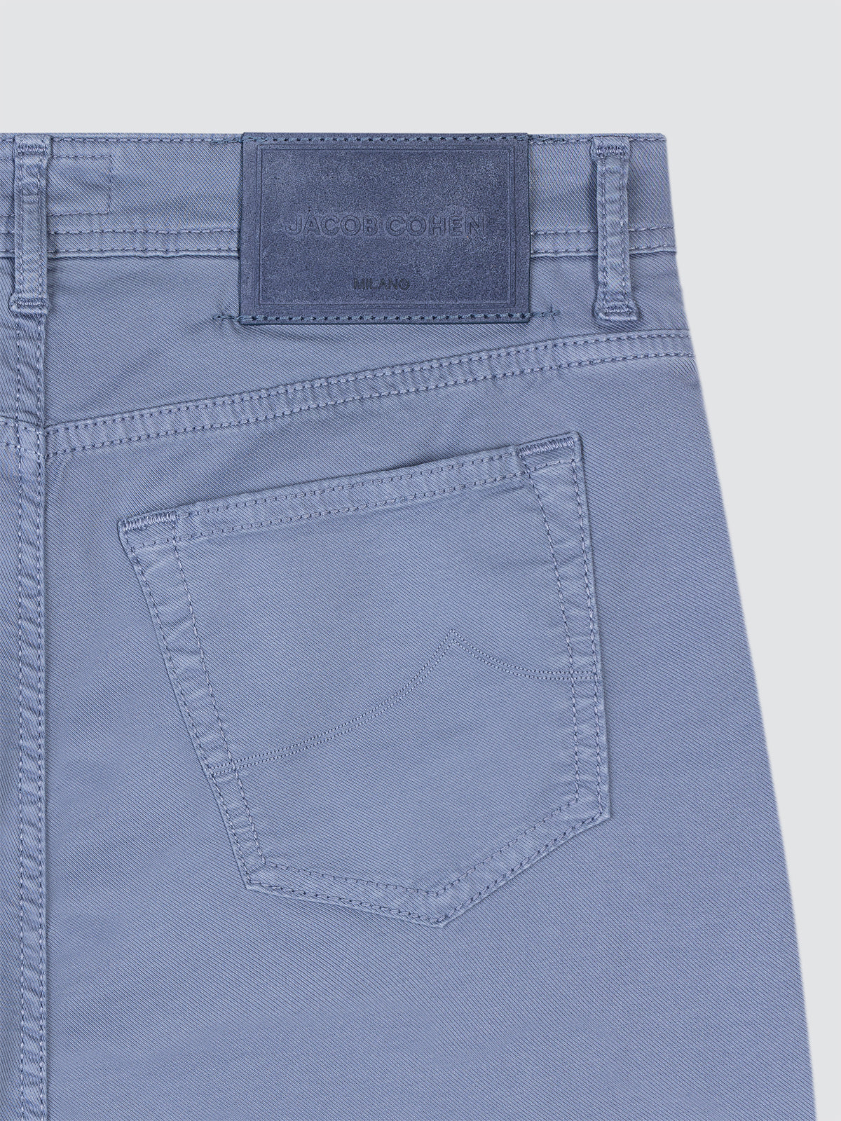 Close-up of lilac blue jeans with a pocket and brand label on a light gray background