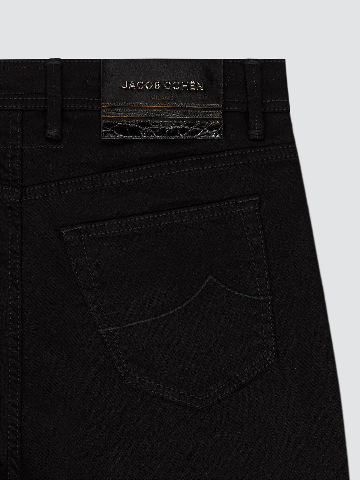 Close-up of the back waistband and pocket of black denim jeans by Jacob Cohen, showing the brand label and stitching details against a light gray background.