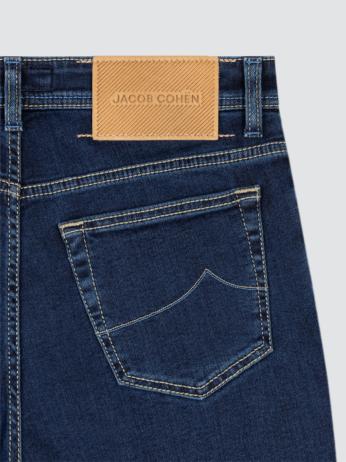 Close-up of blue jeans with a Jacob Cohen label on a light gray background