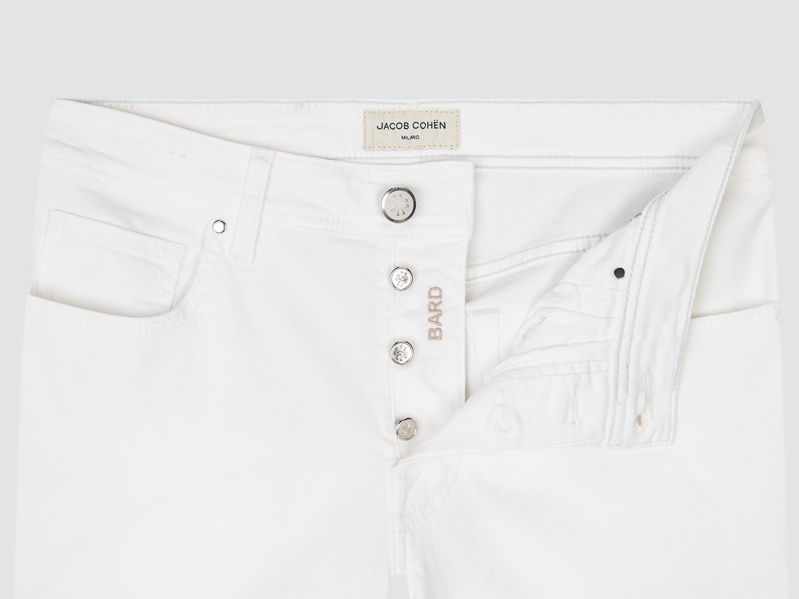 Close-up of white TWILL jeans showing the waistband, button closure, pocket, and a small gold-tone embroidered BARD logo on the side.