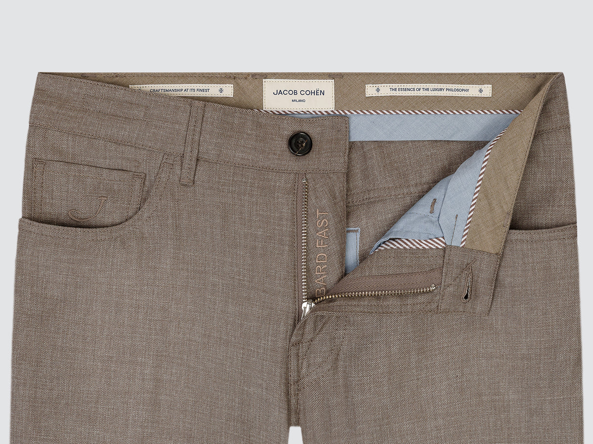 Close-up of a pair of tailored trousers shown flat against a light gray background, with the front waistband, button, zip fly, pockets, and interior lining visible. The label reads Jacob Cohen.