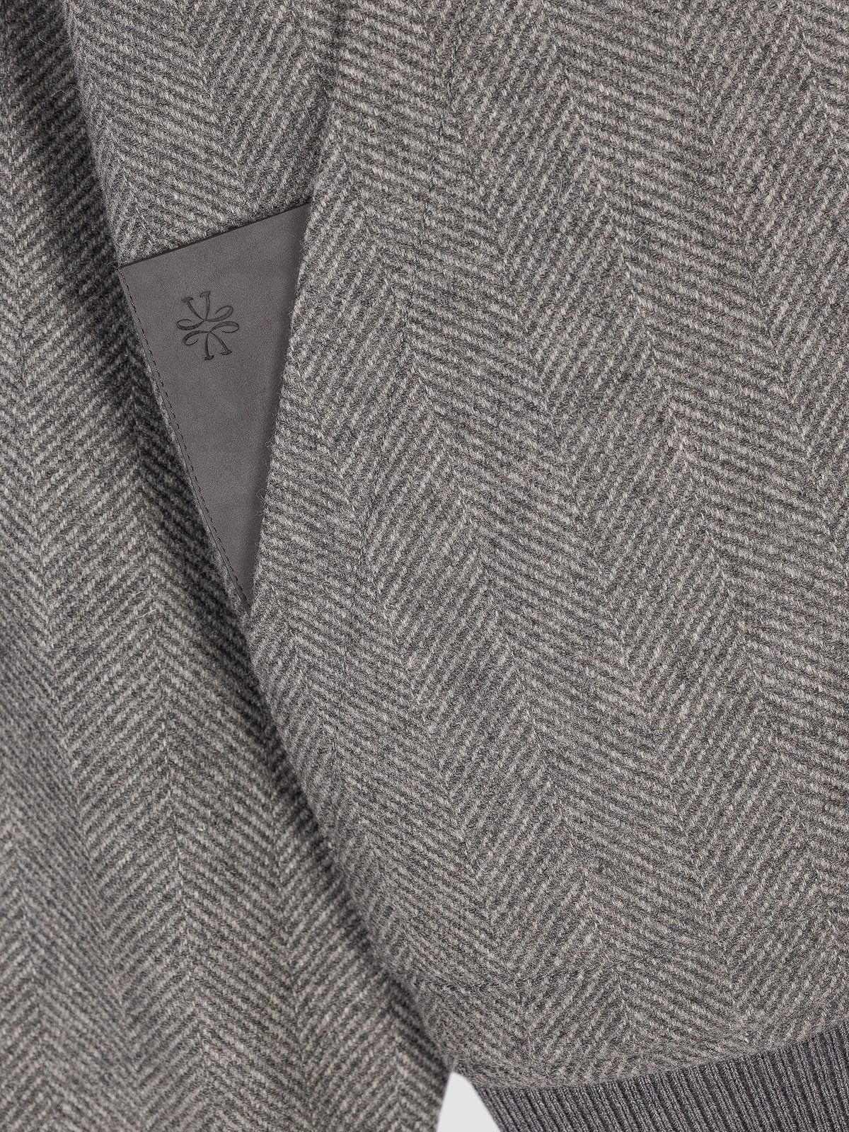 Close-up of a gray herringbone tweed fabric with a dark gray inner label featuring a small embroidered monogram.