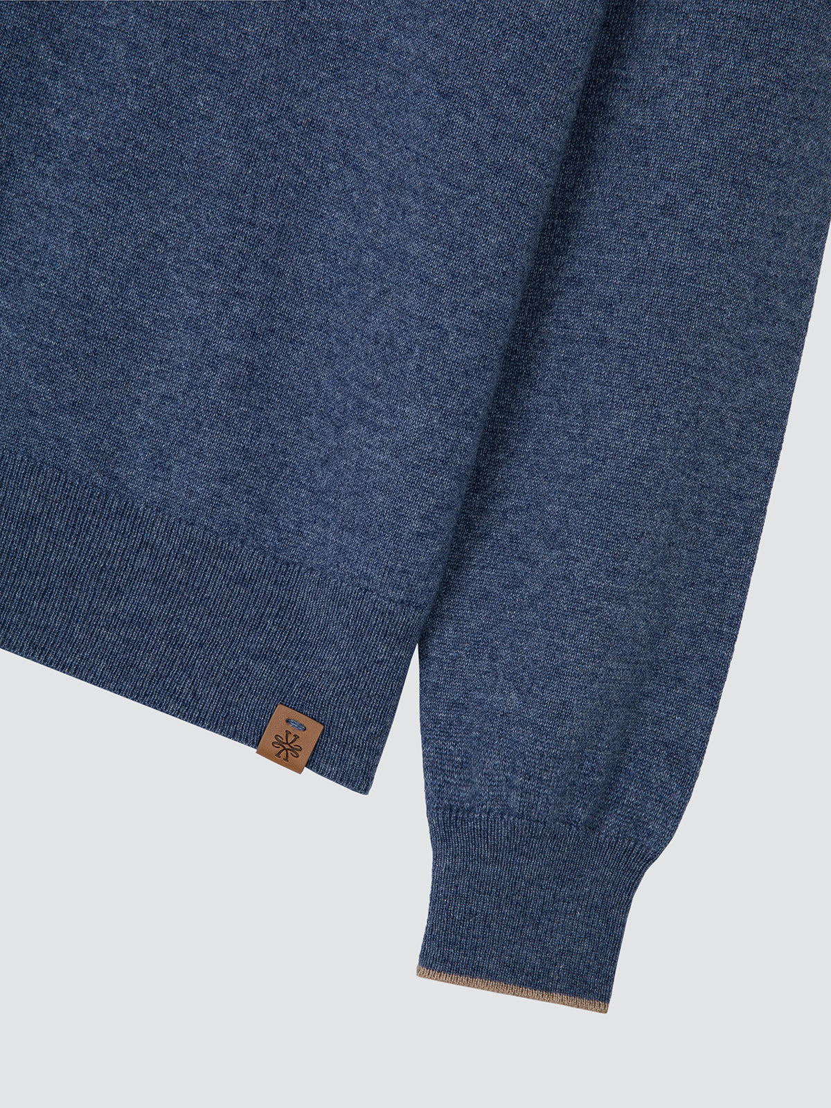 Close-up of a heathered blue knit sweater with ribbed cuffs and hem, featuring a small brown brand tag near the lower cuff.