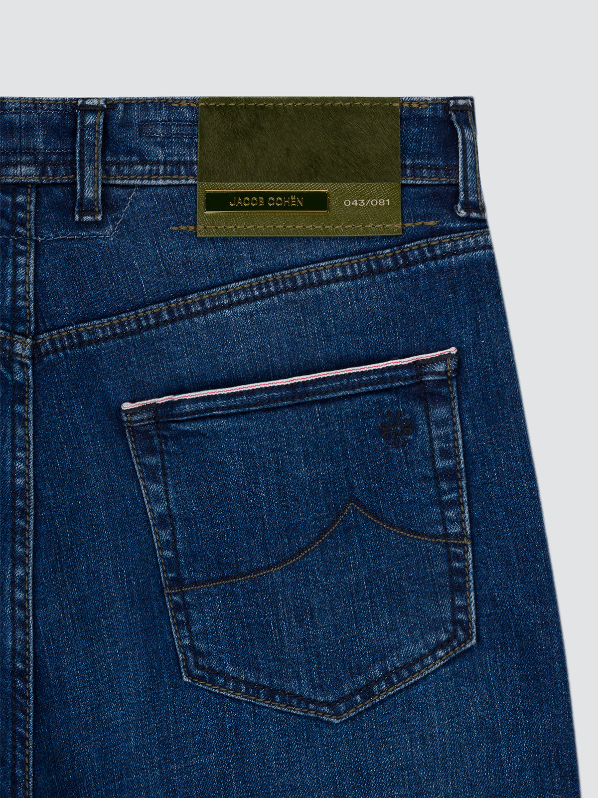 Close-up of the back waistband and rear pocket of blue denim jeans, showing a green leather patch with JACOB COHEN limited edition with red line