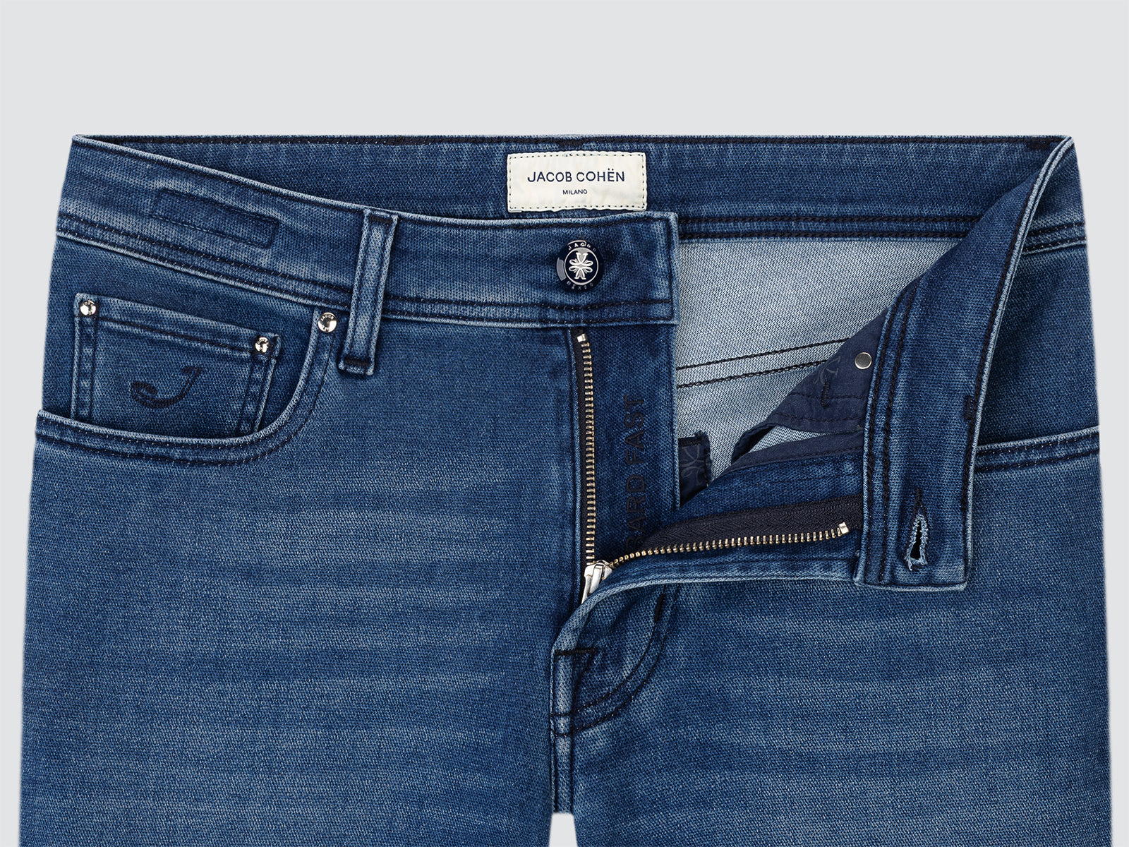 Blue jeans with a visible brand Jacob Cohen label on a light gray background