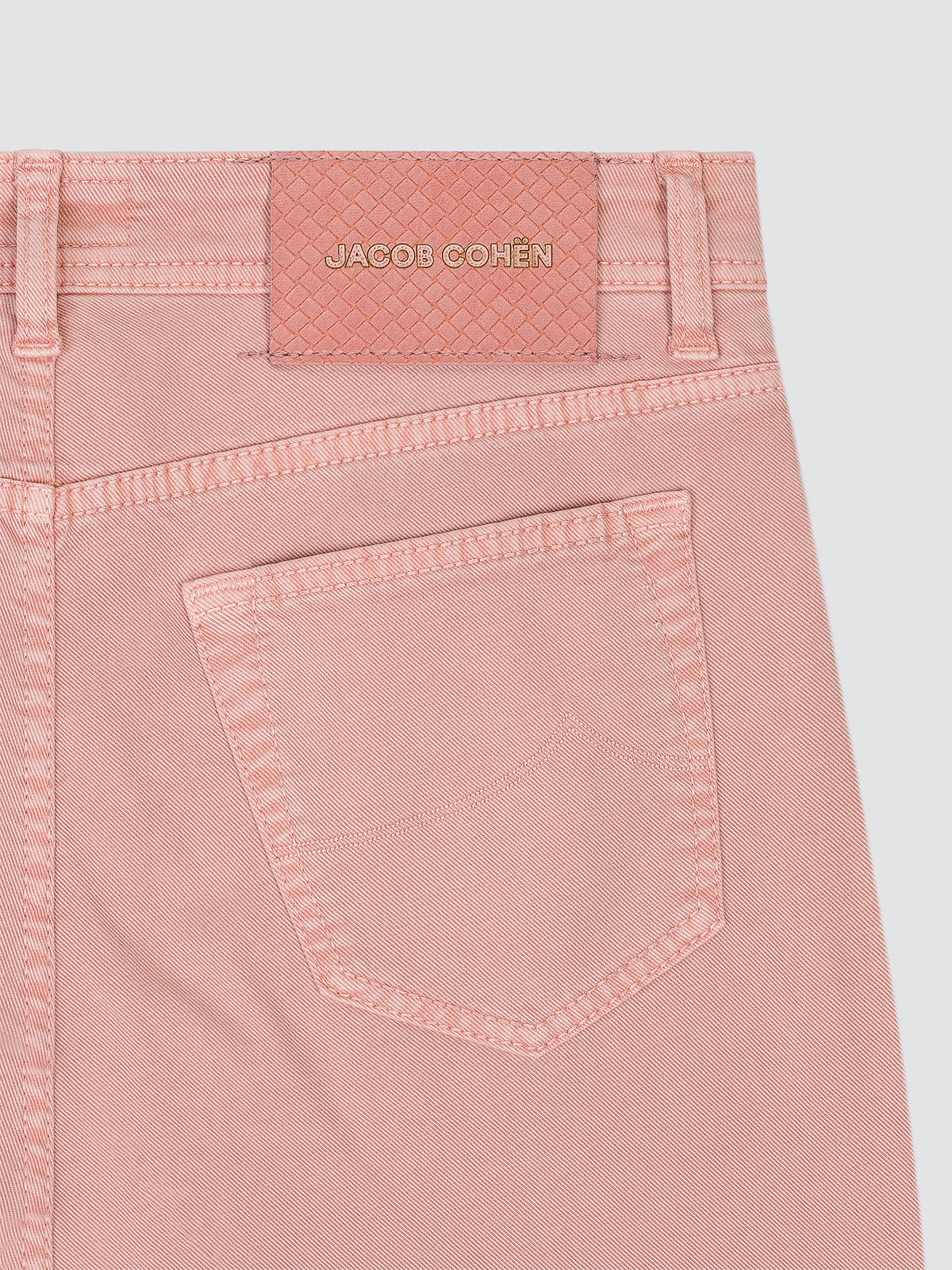 Close-up of the back waistband and pocket of light pink denim jeans by Jacob Cohen, showing the brand patch and stitching on a light gray background.