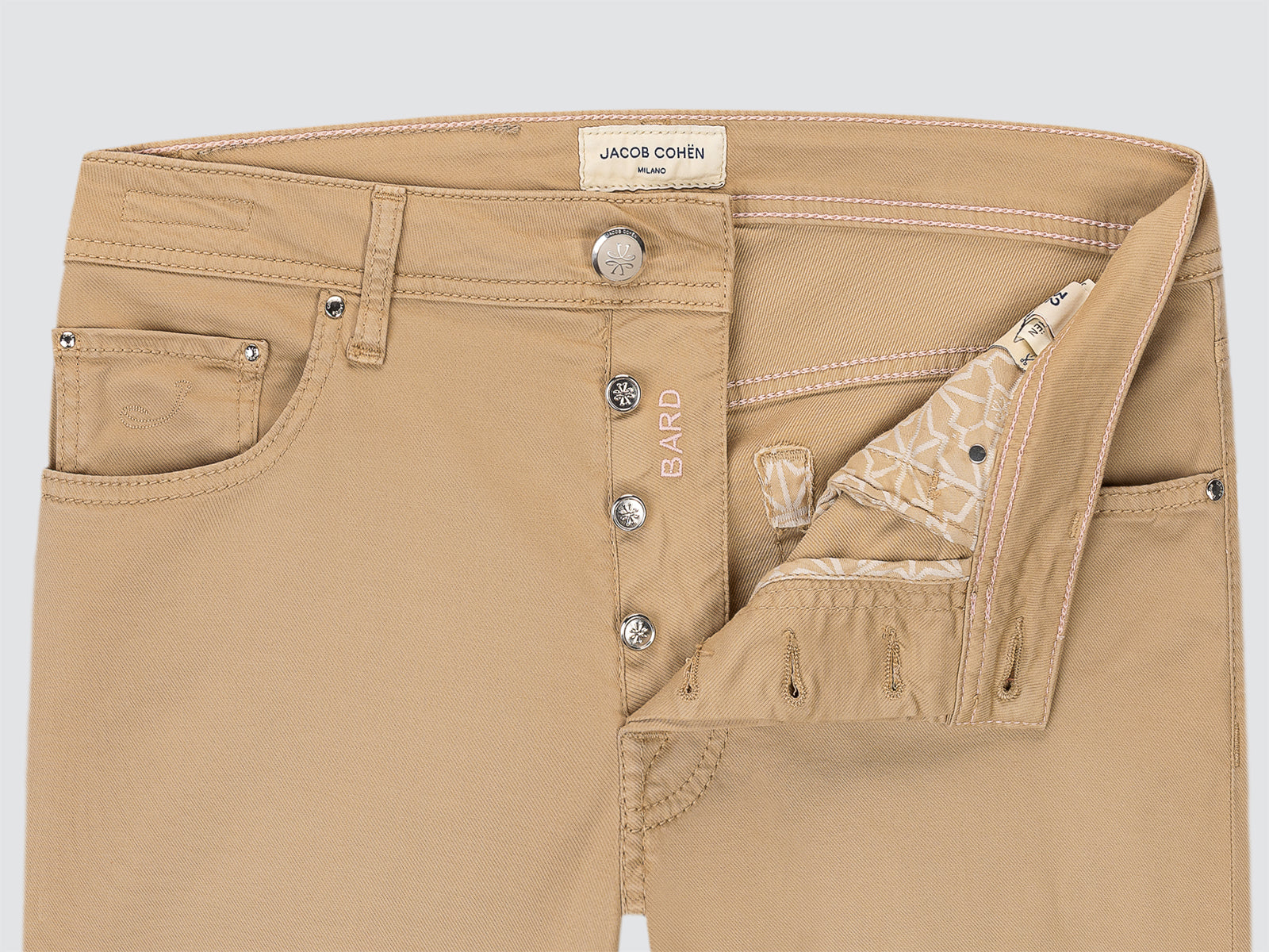 Close-up of beige pants with visible branding on a light gray background