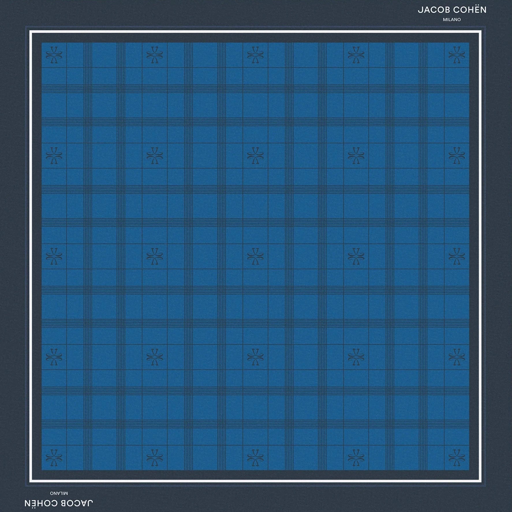 A square scarf featuring a blue and navy tartan plaid pattern, framed by a dark navy border with white text reading 'JACOB COHEN NEW YORK' at the top and bottom, set against a solid beige background.