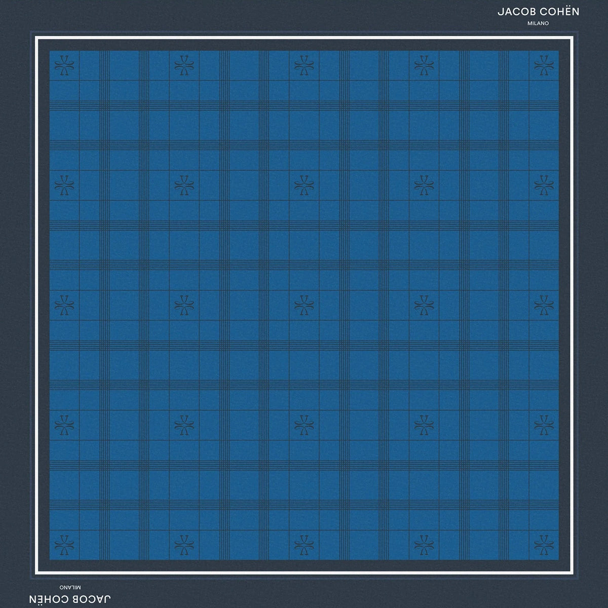 A square scarf featuring a blue and navy tartan plaid pattern, framed by a dark navy border with white text reading 'JACOB COHEN NEW YORK' at the top and bottom, set against a solid beige background.