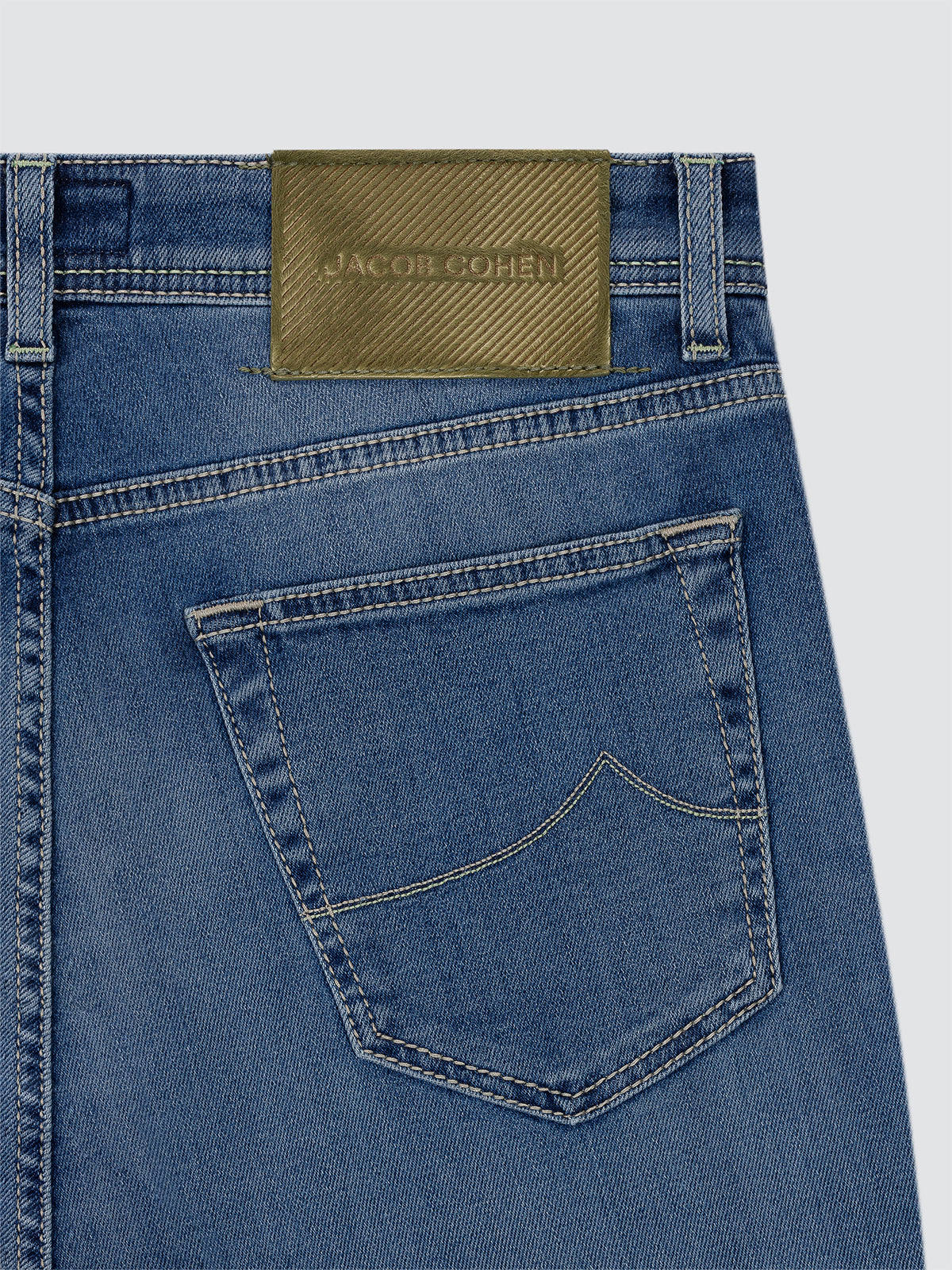 Close-up of blue jeans with a Jacob Cohen label on a light gray background