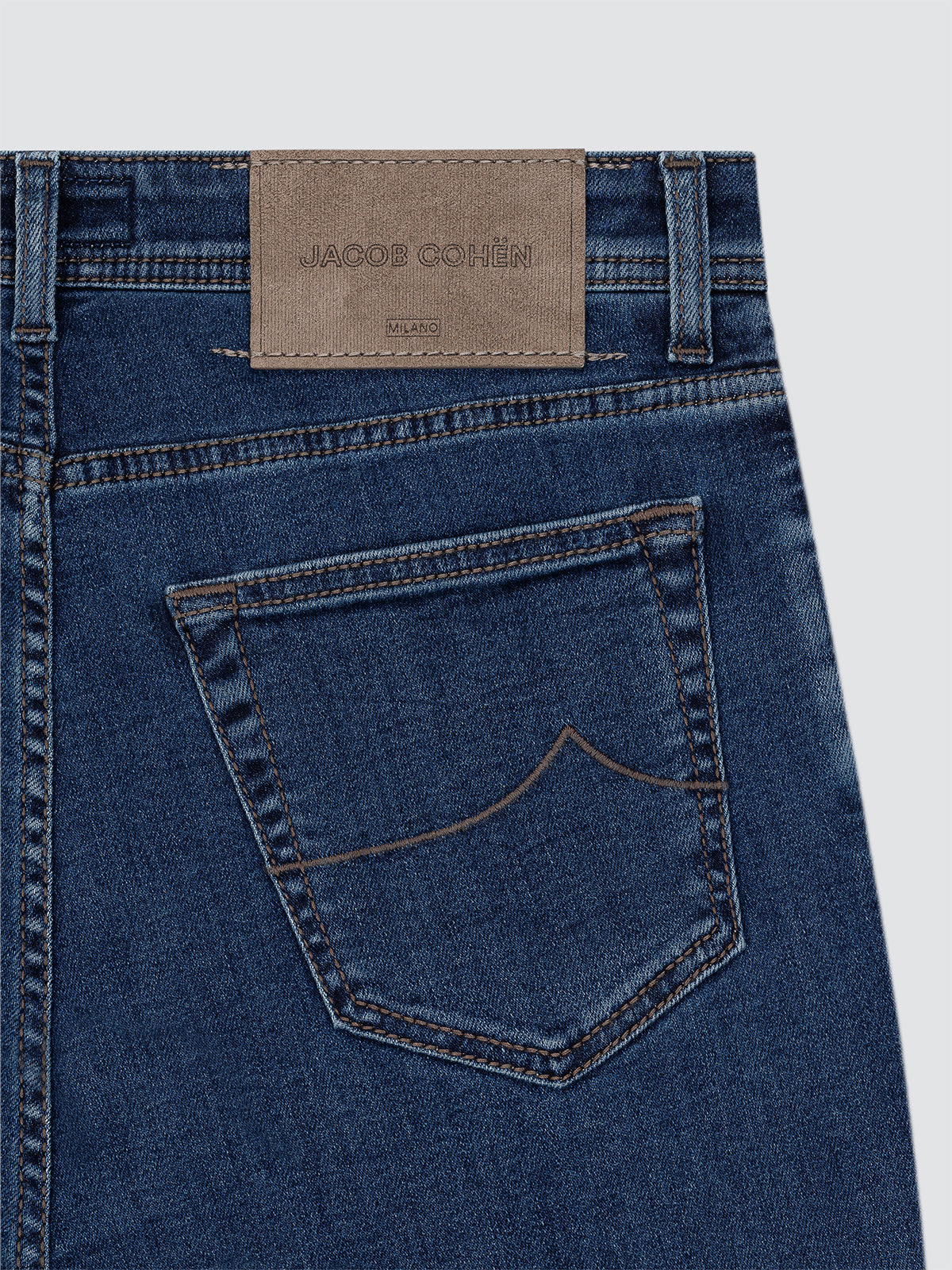 Close-up of blue jeans with a brand label BACK PATCH Jacob Cohën on a light gray background