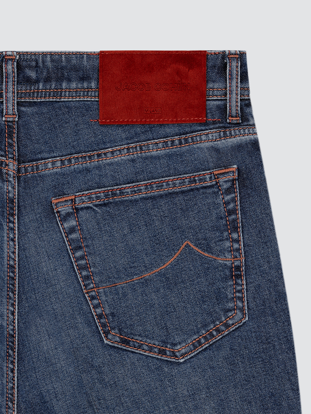 Close-up of blue jeans Jacob Cohën Nick with a red patch on a light gray background