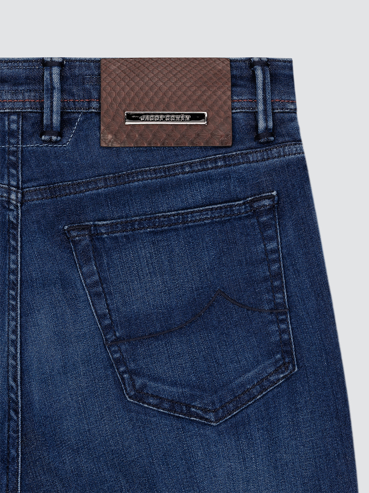 Close-up of blue jeans Jacob Cohen with a brand label Pithon brown on a light gray background