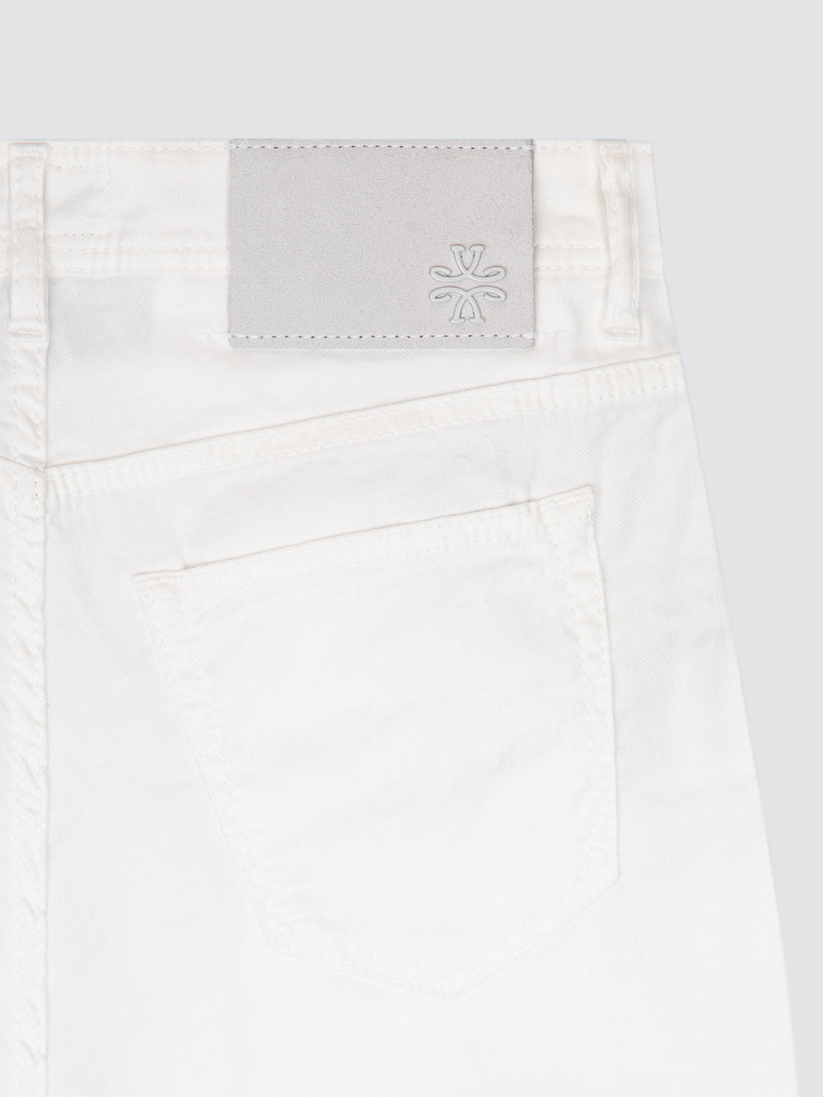 Close-up of a white linen pants waistband with a brand label Jacob Cohën on a light gray background