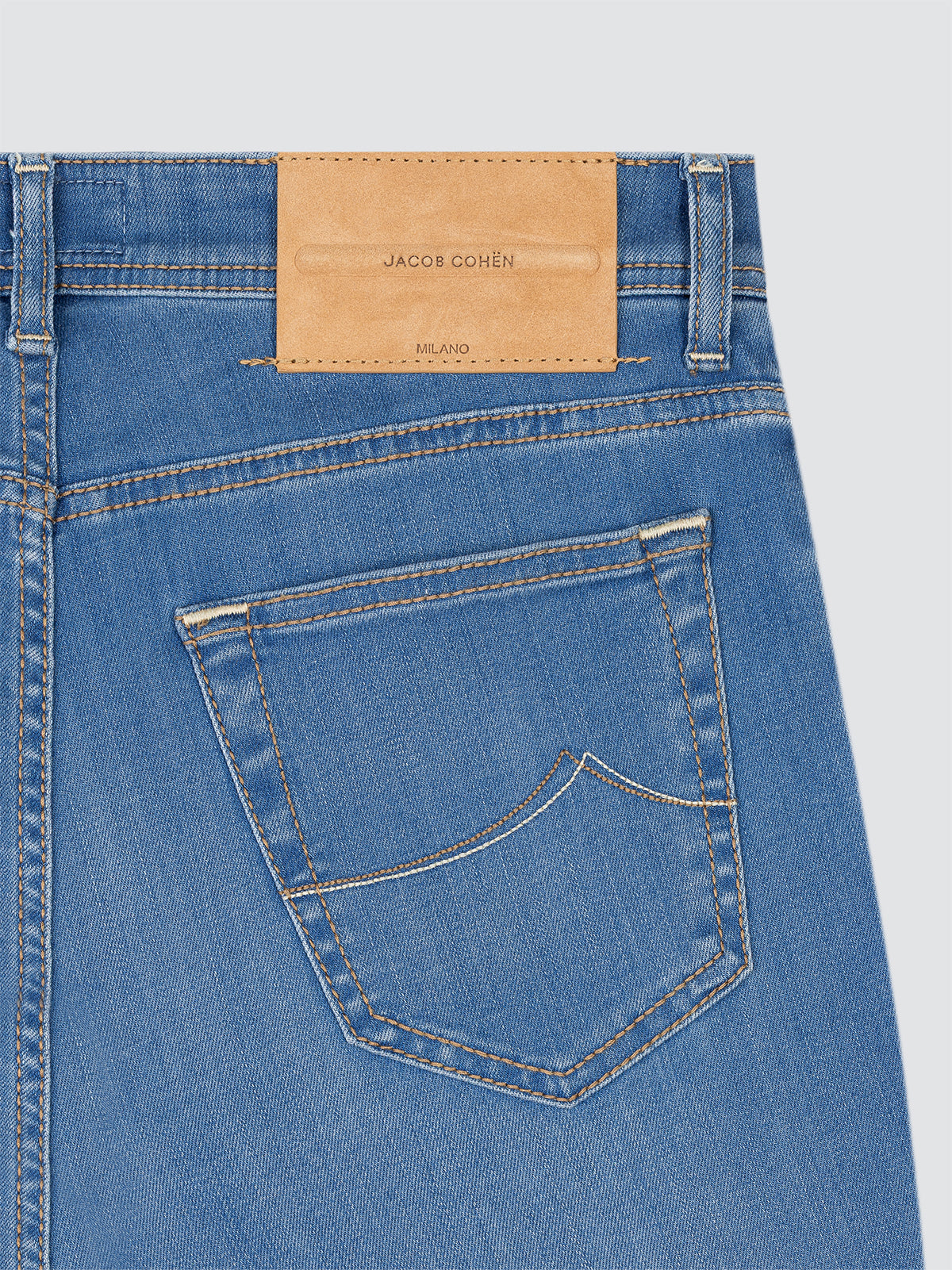 Close-up of light blue jeans with a brand label Jacob Cohen on a light gray background