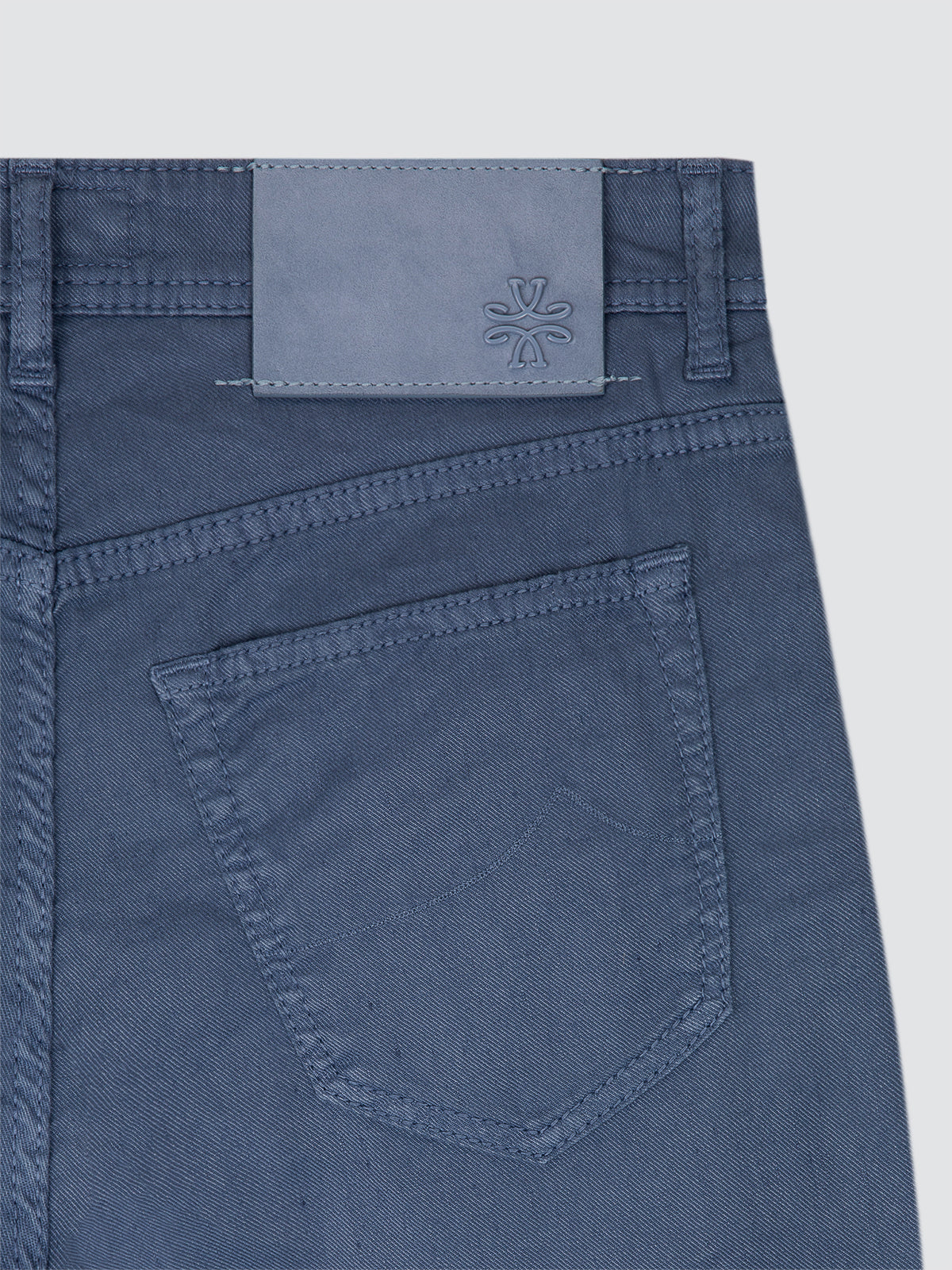 Close-up of colony blue linen jeans with a brand logo on the back pocket against a light gray background by Jacob Cohën