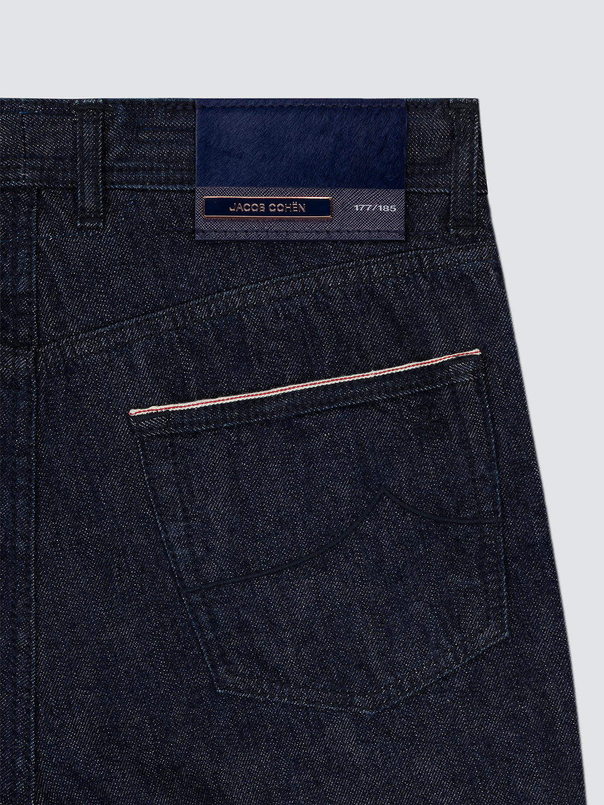 Close-up of the back waistband and pocket area of dark indigo limited denim jeans, showing a visible Jacob Cohen brand label and contrast stitching.