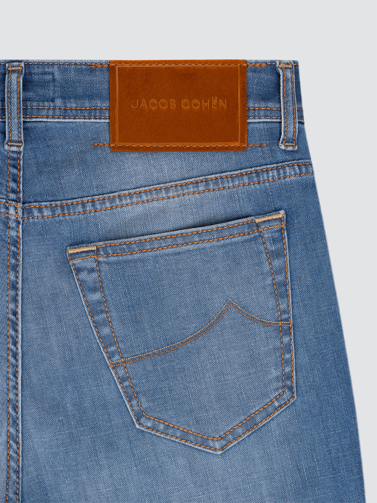Close-up of blue jeans with a brown Jacob Cohen label on a light gray background