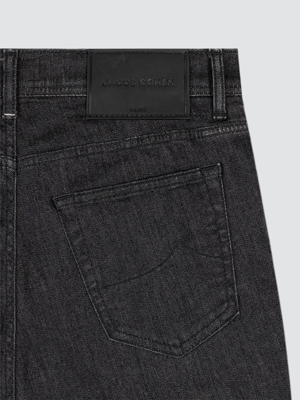 Close-up of black denim jeans with a brand label Jacob Cohen on a light gray background