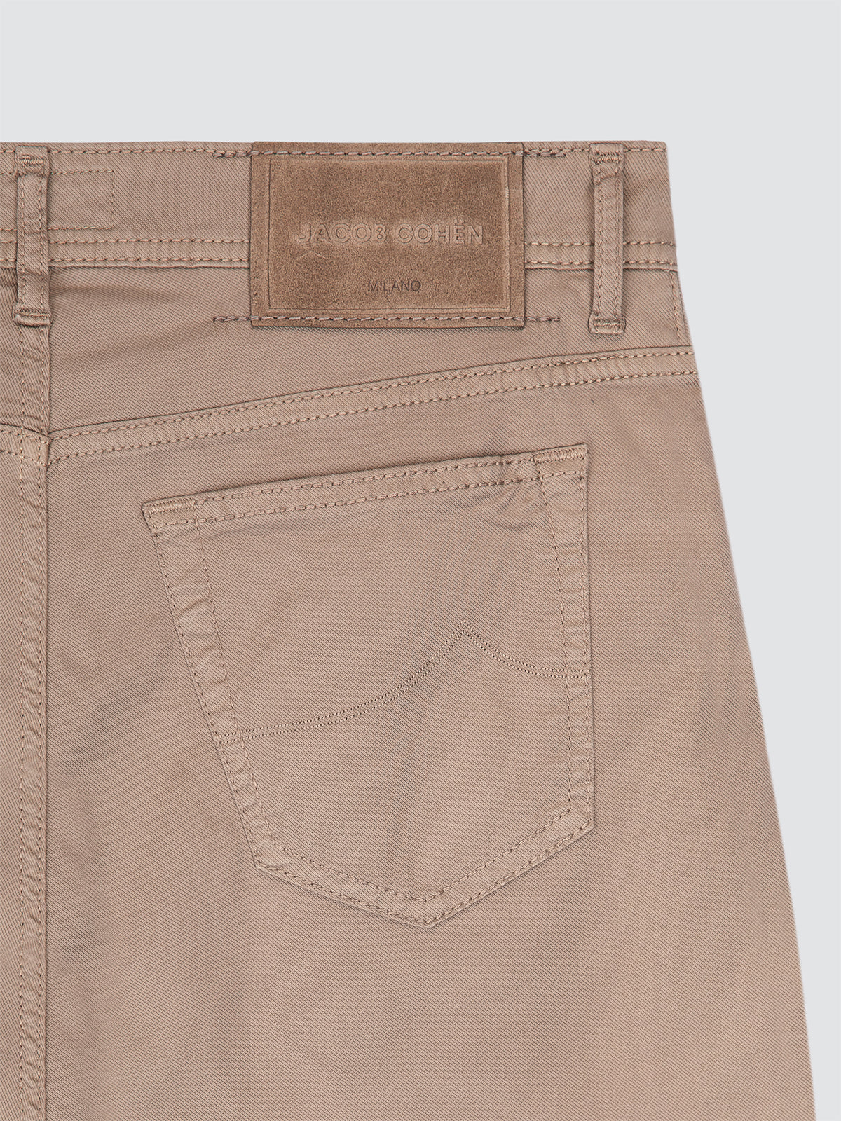 Close-up of beige pants with a brand label Jacob Cohen on a light gray background