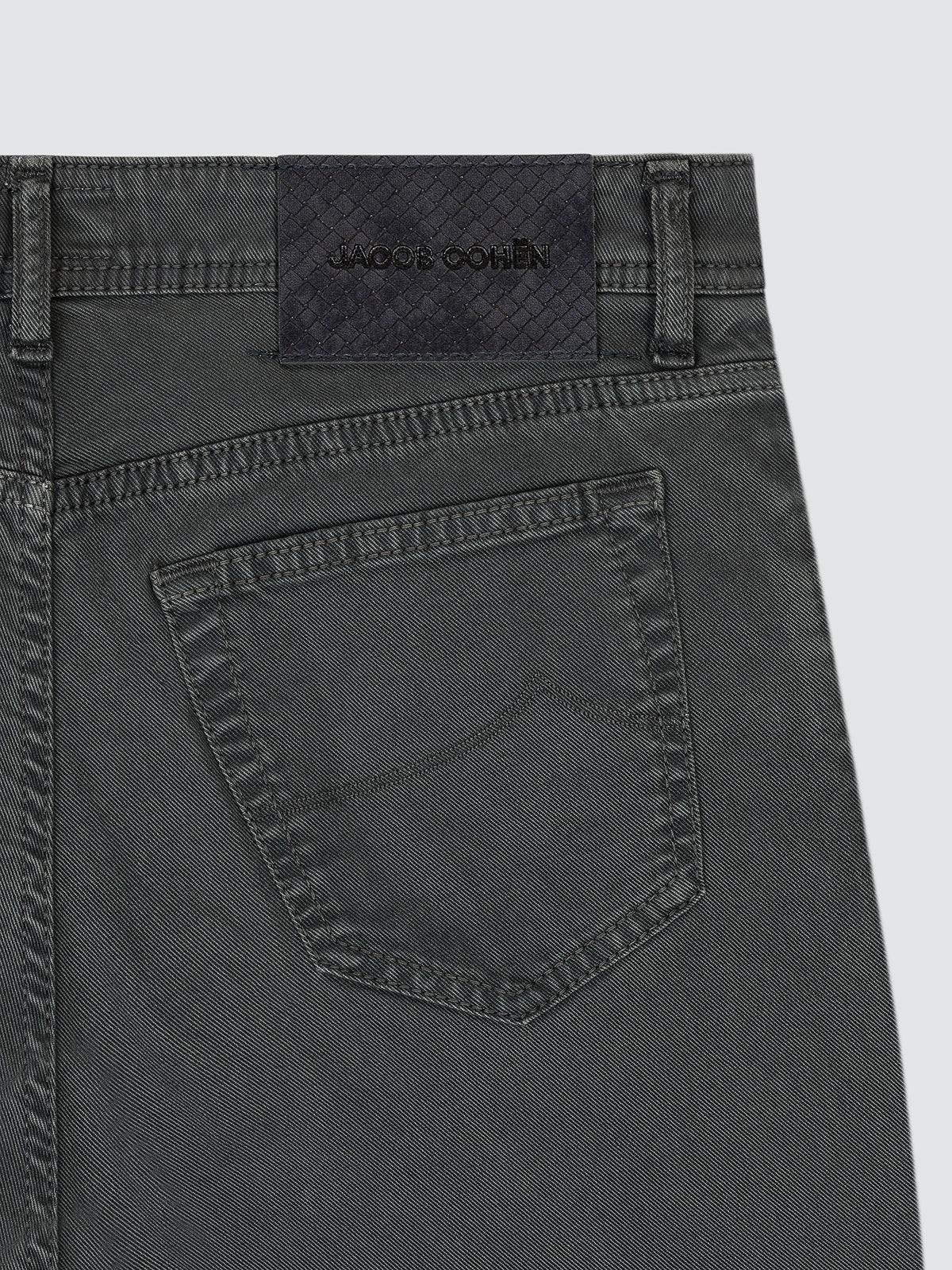 Close-up of the back waistband and pocket of olive green denim jeans, showing a dark brown leather patch with the brand name 'JACOB COHEN' stitched on it.