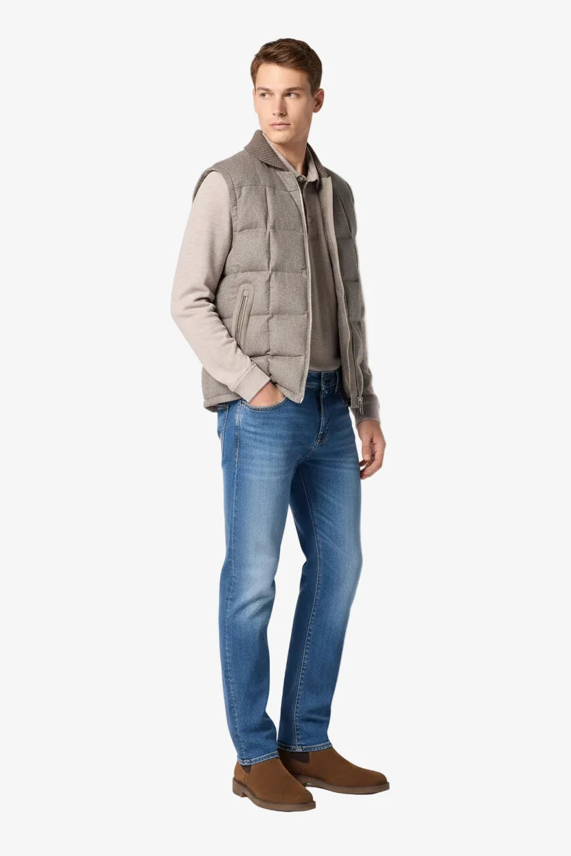 Man wearing a gray vest over a shirt with blue jeans and brown shoes on a white background
