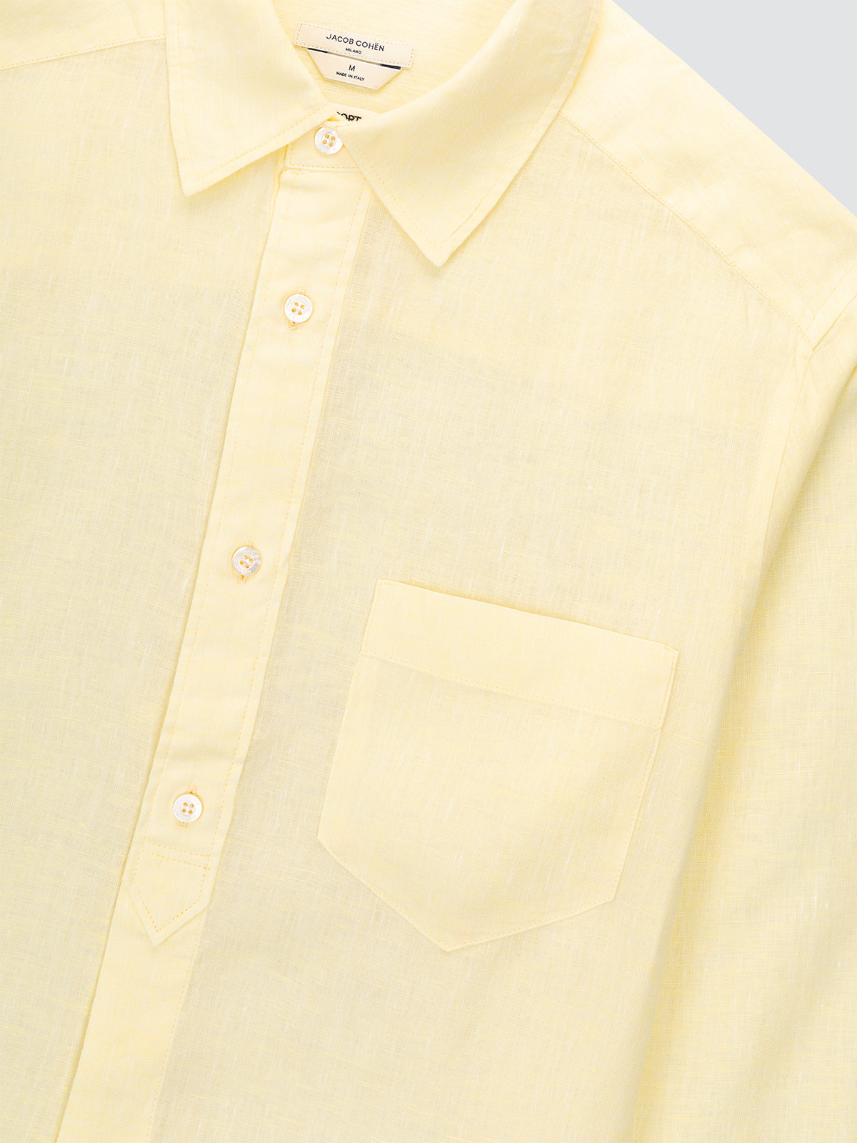Close-up of a light yellow button-up shirt with a pocket on a light gray background