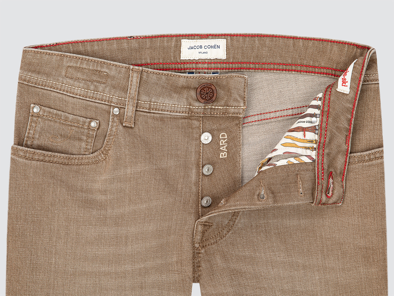 Close-up of brown jeans with visible branding on a light gray background
