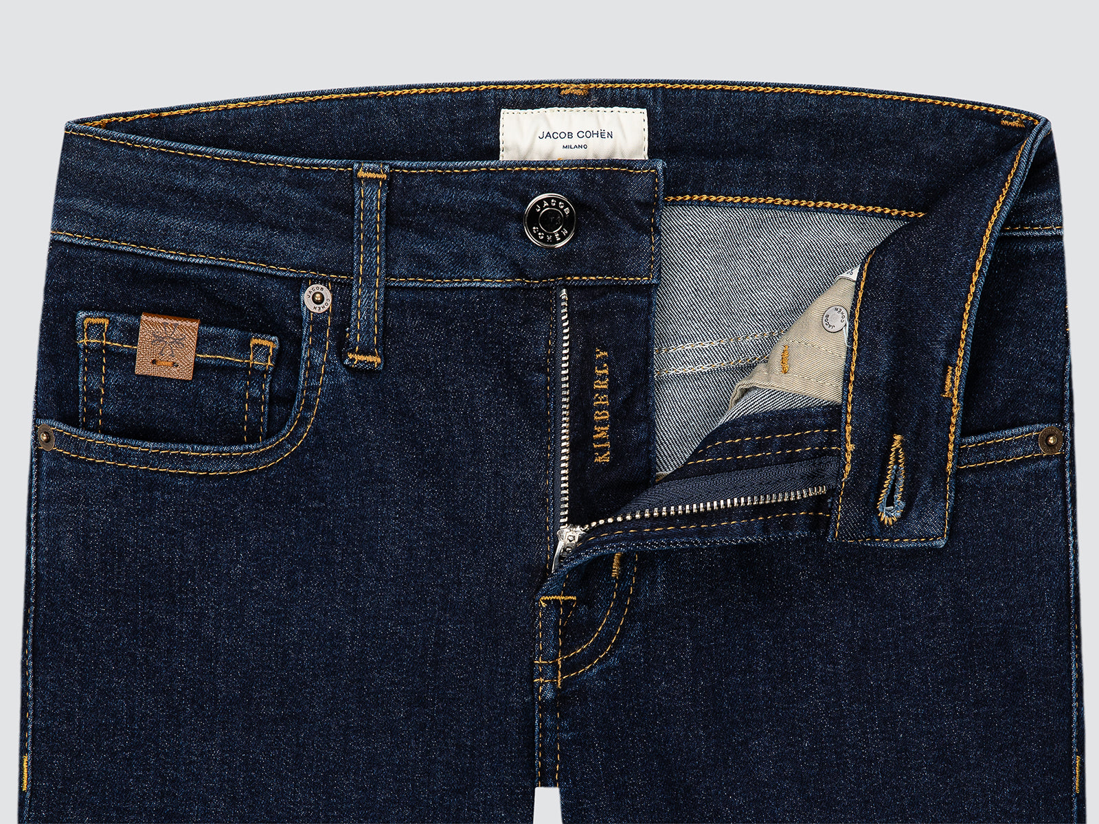 Close-up of dark blue jeans with brand labels on a light gray background