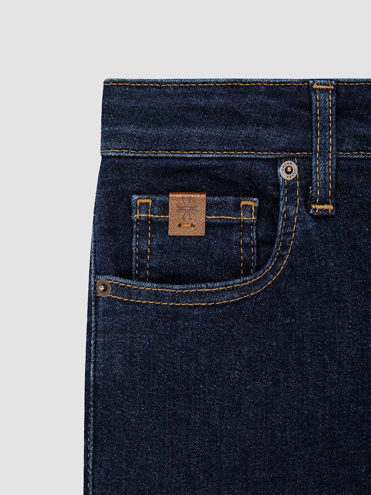 Close-up of dark blue jeans with a brand logo Jacob Cohën on the pocket against a light gray background