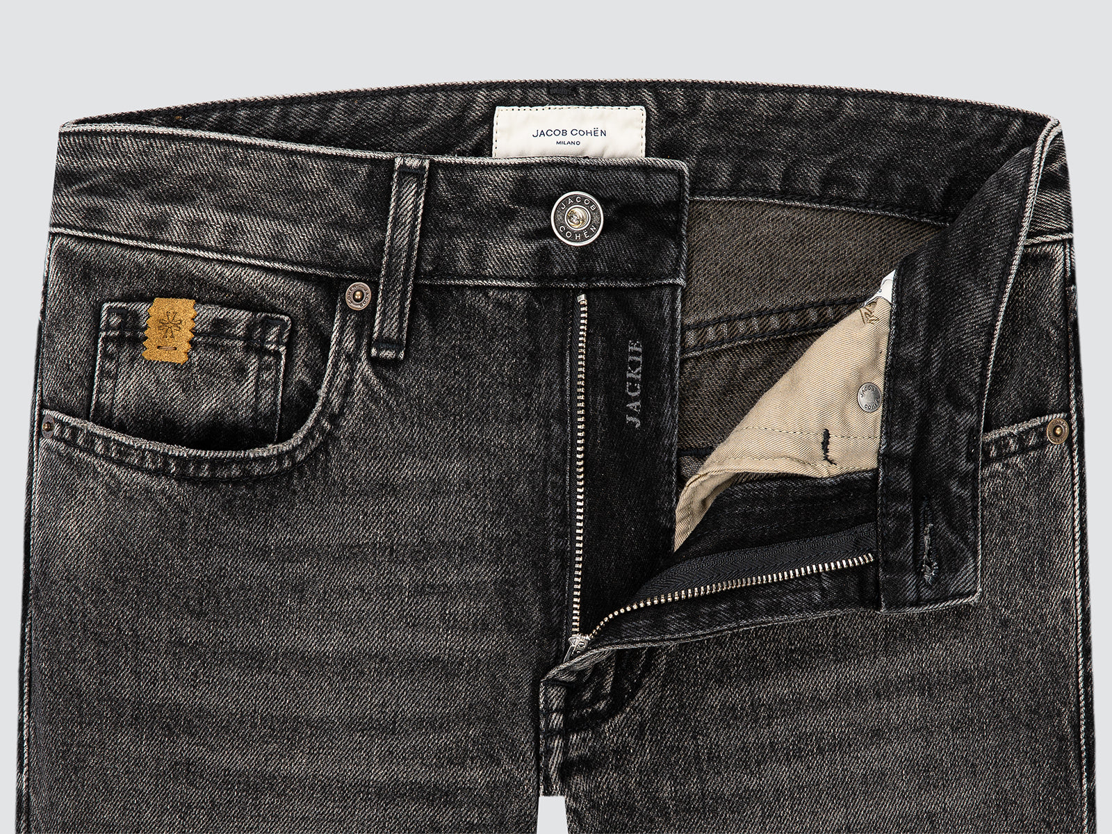Close-up of black jeans with a visible brand label on a light gray background