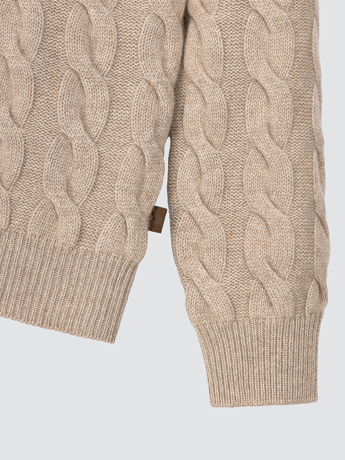 Close-up of a beige cable knit sweater on a light gray background