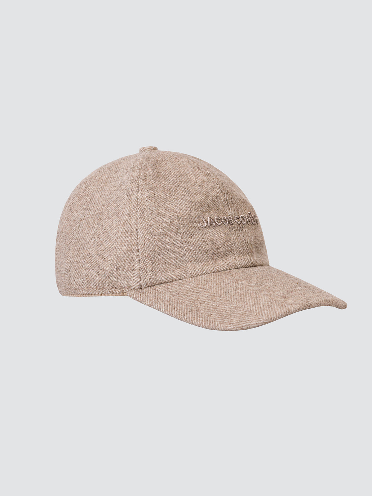 A beige herringbone textured baseball cap with 'JACOB COHEN' embroidered on the side, shown against a solid light gray background.