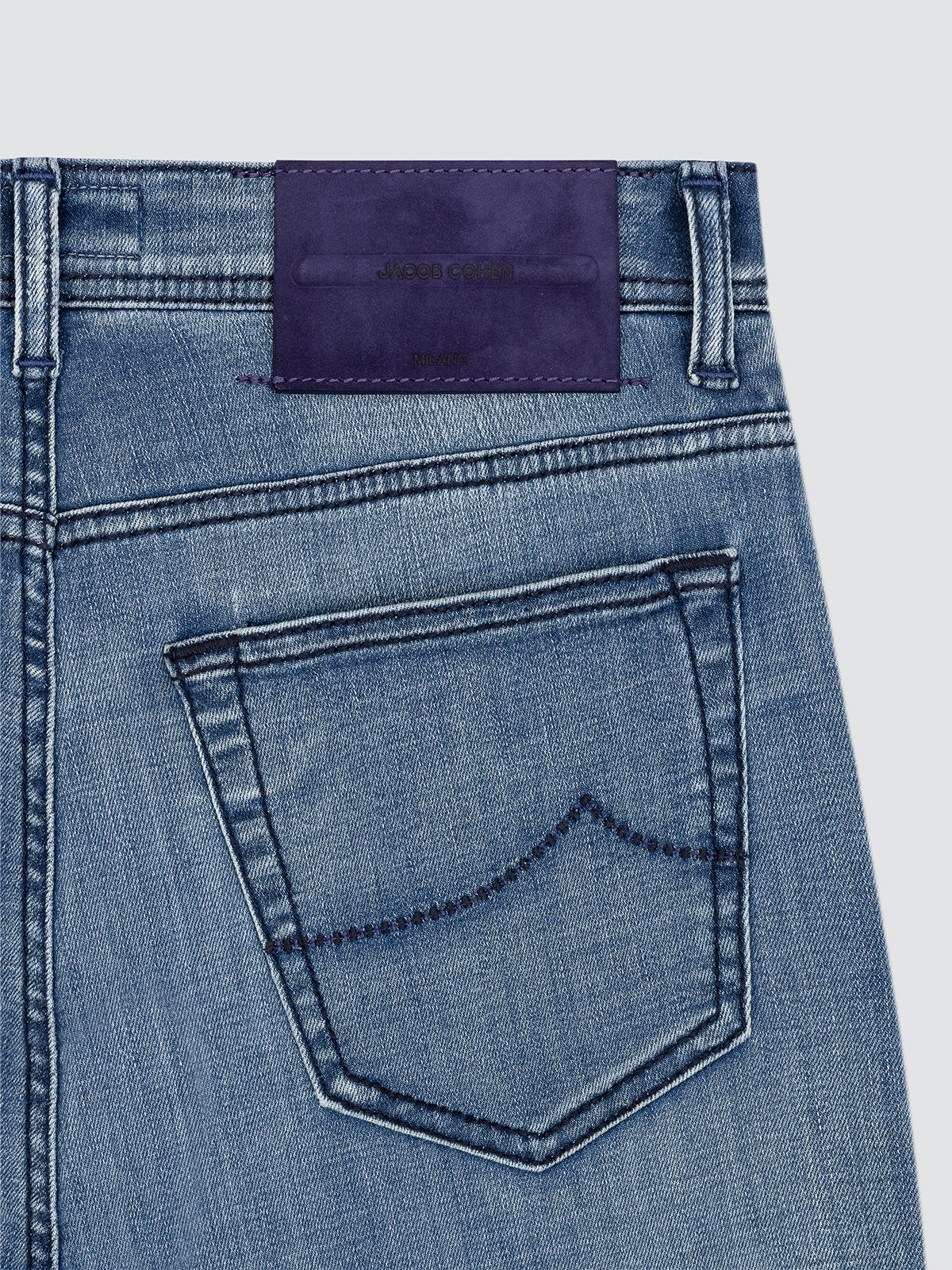 Close-up of blue denim jeans with a purple label on a light gray background