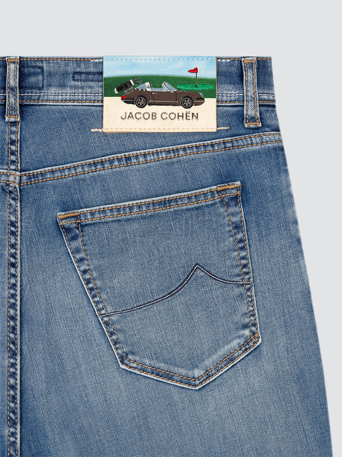 Close-up of blue jeans with a Jacob Cohen label  GOLF AND PORSCHE on a light gray background
