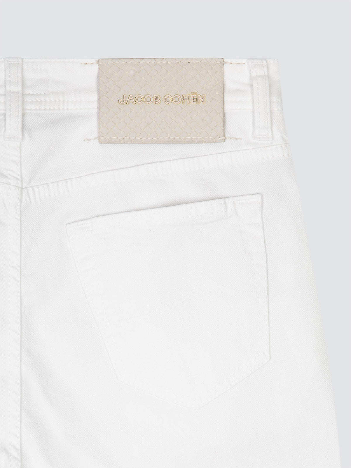 Close-up of white twill 5 pockets pants showing the back waistband with a beige JACOB COHEN brand patch and a back pocket, on a light gray background.