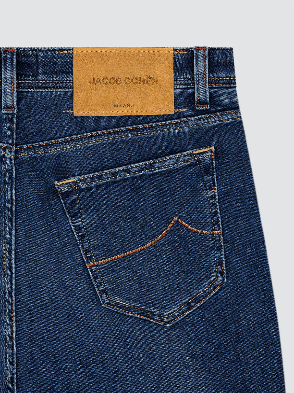 Close-up of blue jeans with a Jacob Cohen label on a light gray background