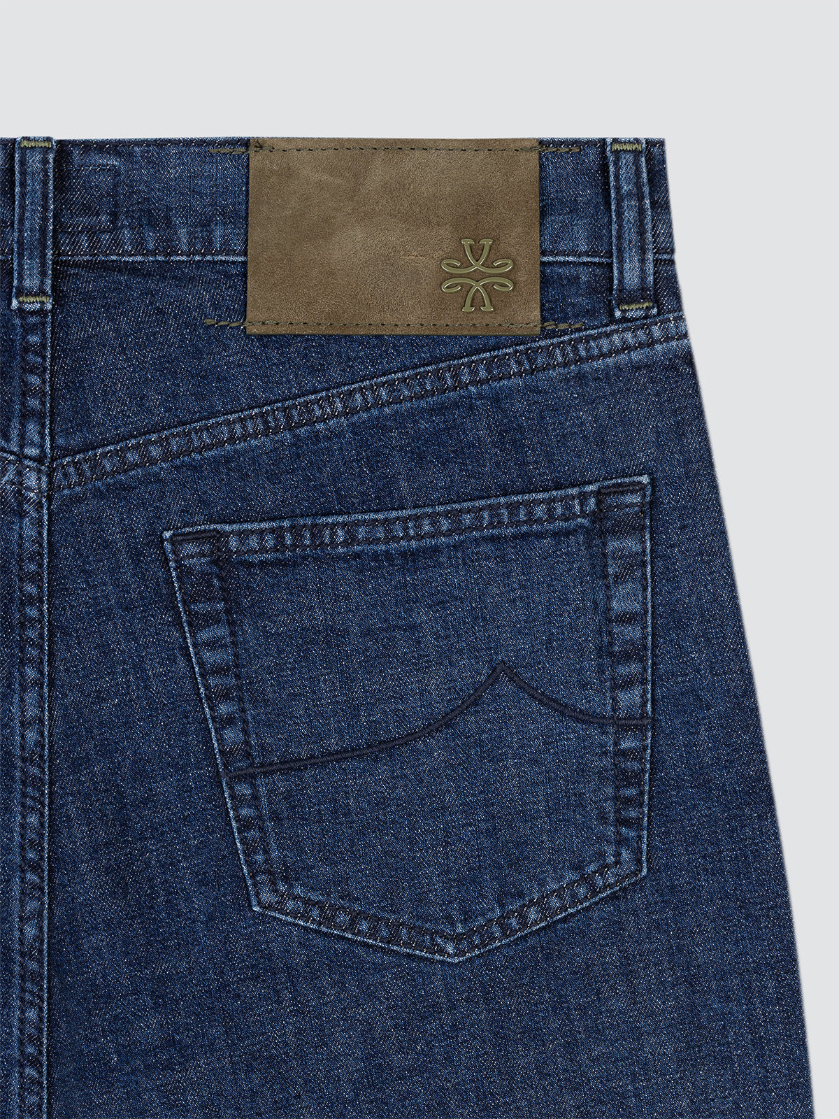 Close-up of blue denim jeans with a brown leather patch Jacob Cohen on a light gray background