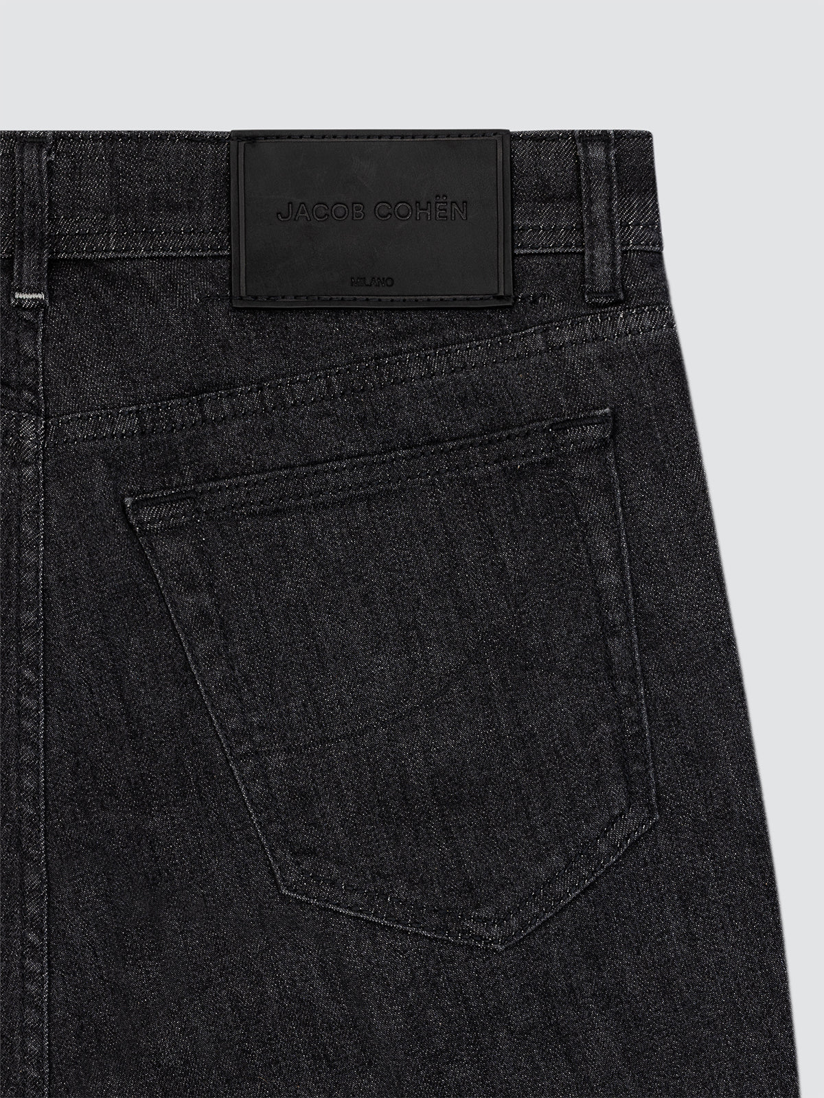 Close-up of black jeans with a brand label on a light gray background