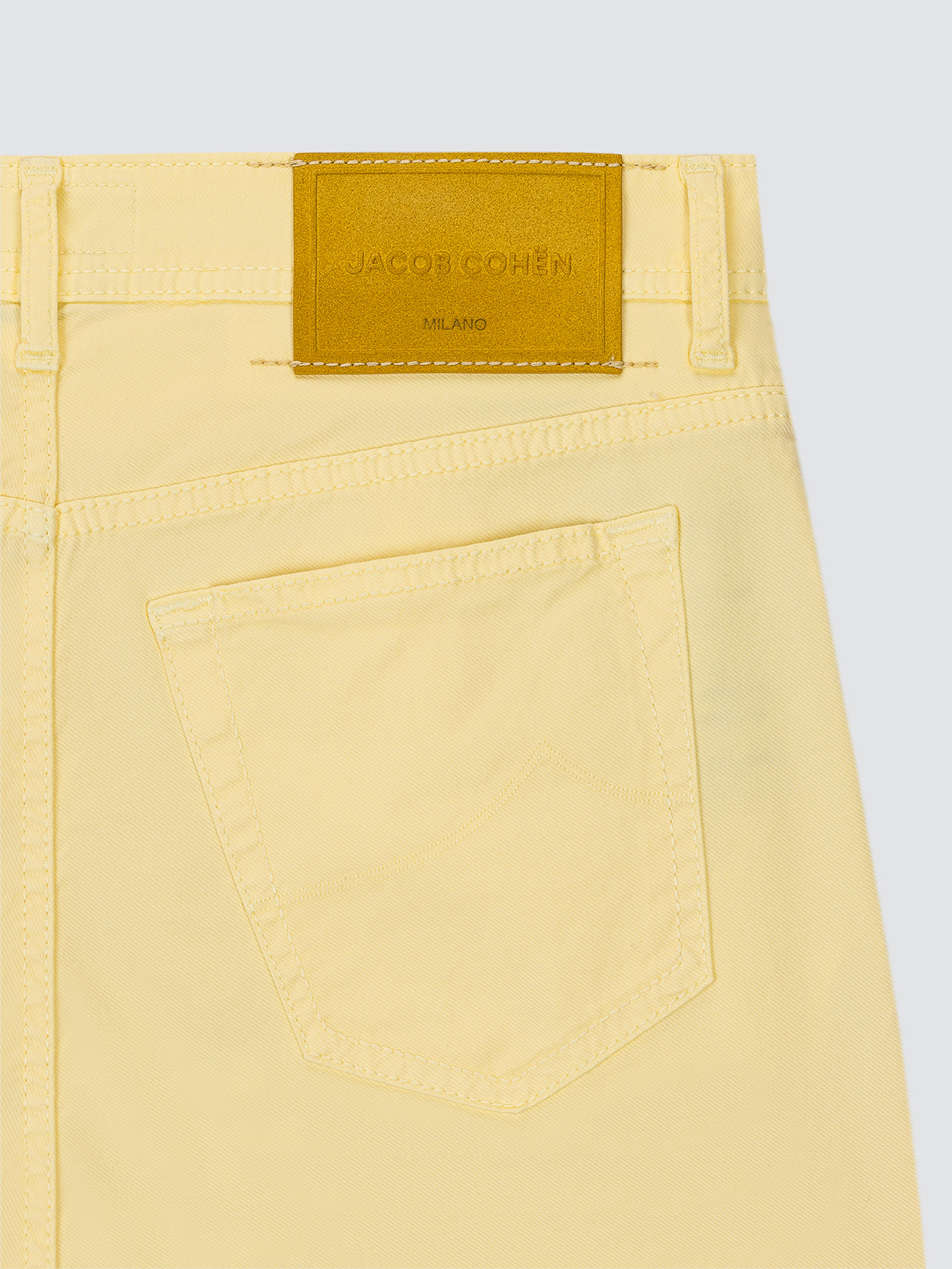 Close-up of yellow 5 POCKETS pants with a brand label on a light gray background