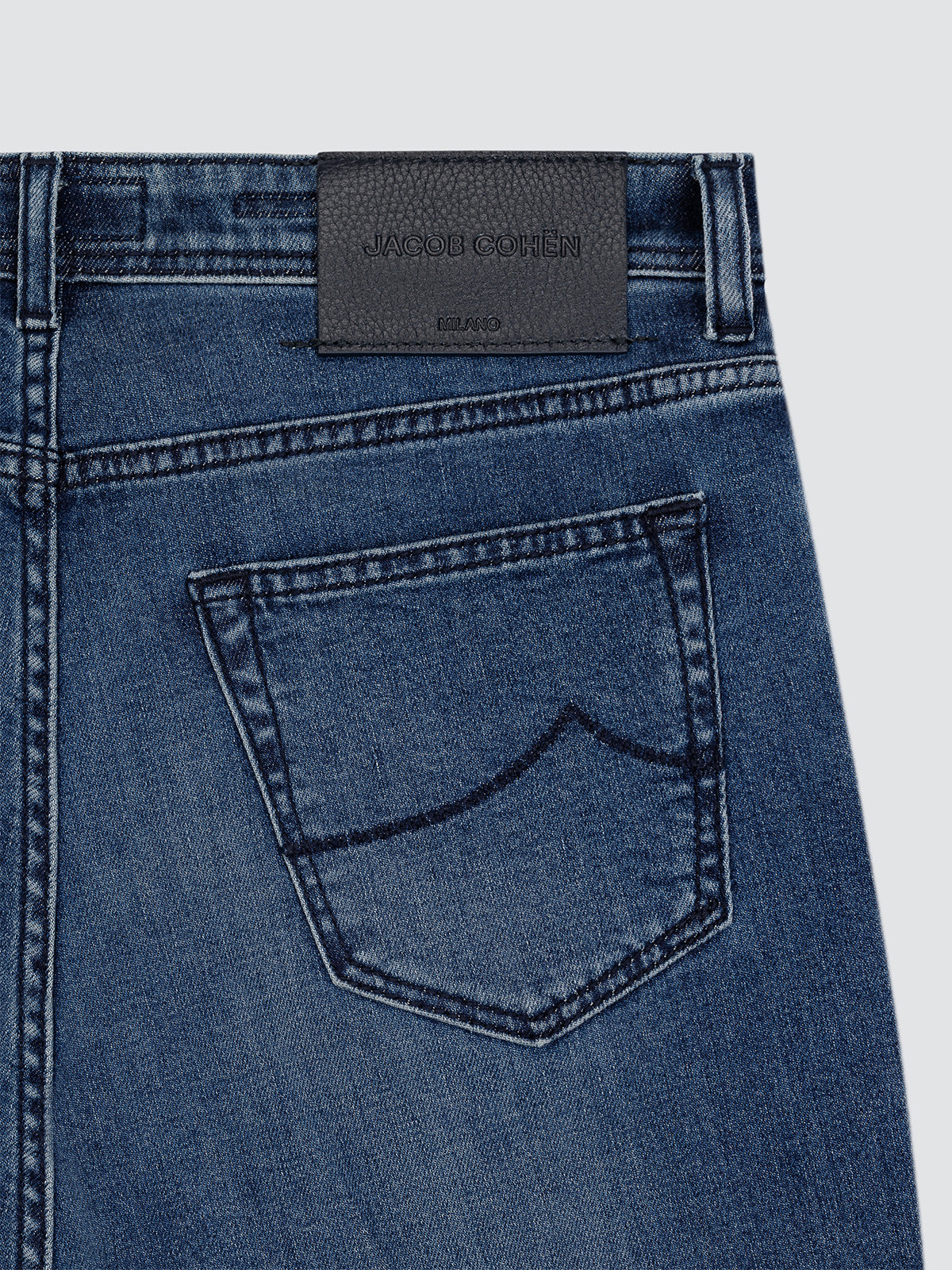Close-up of blue denim cachemire jeans with a brand label Jacob Cohen on a light gray background