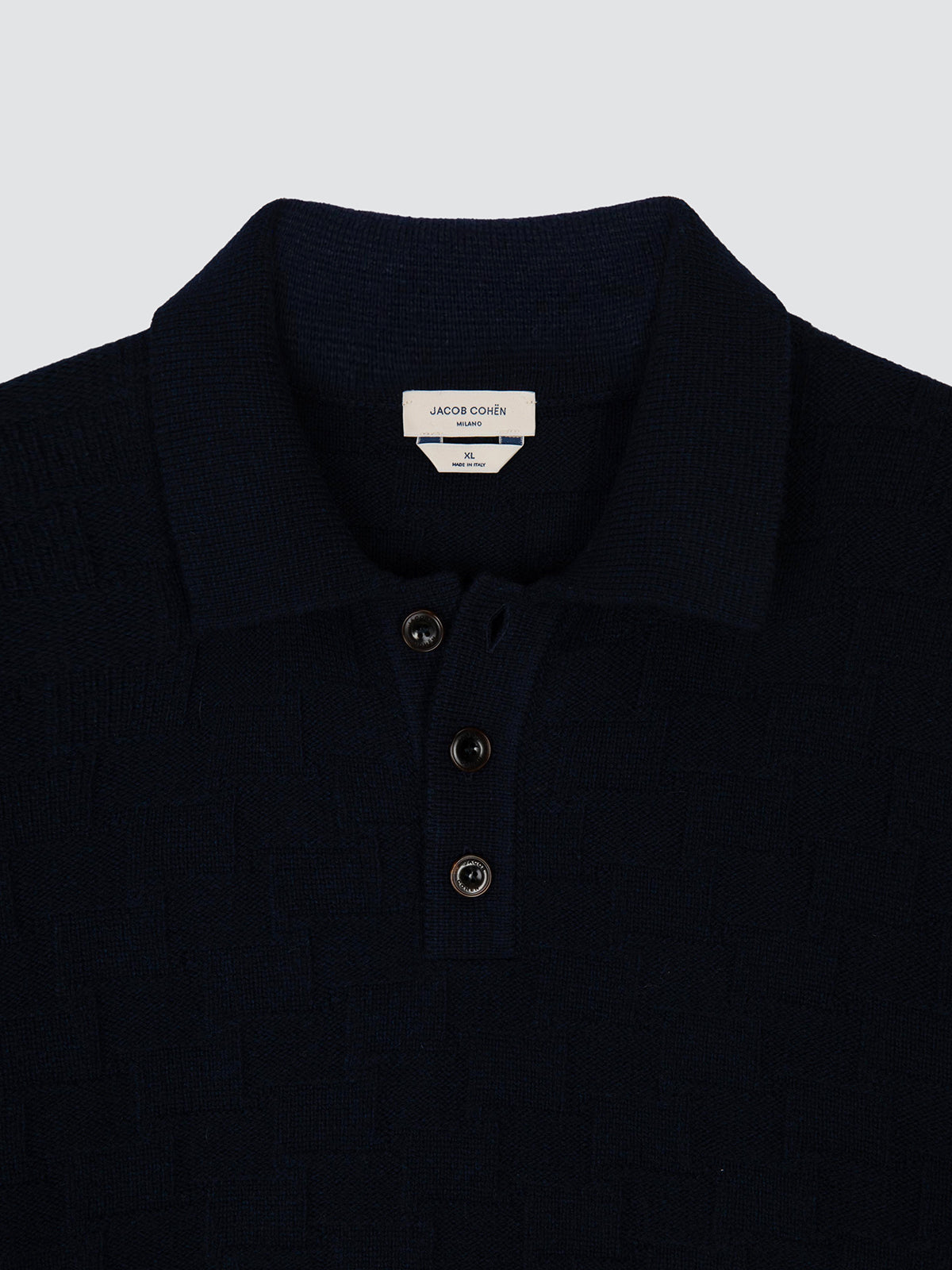 Close-up of a dark navy blue knit polo shirt by Jacques Couiner, featuring a three-button placket and a white neck label.