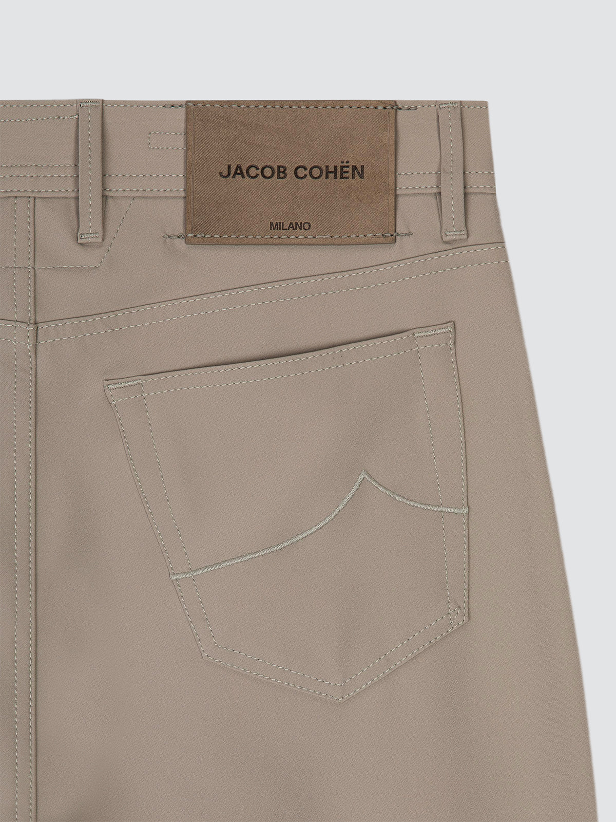Close-up of the back waistband and pocket of a pair of light beige trousers tech microfibre by Jacob Cohen, showing a brown leather brand patch and clean stitching.