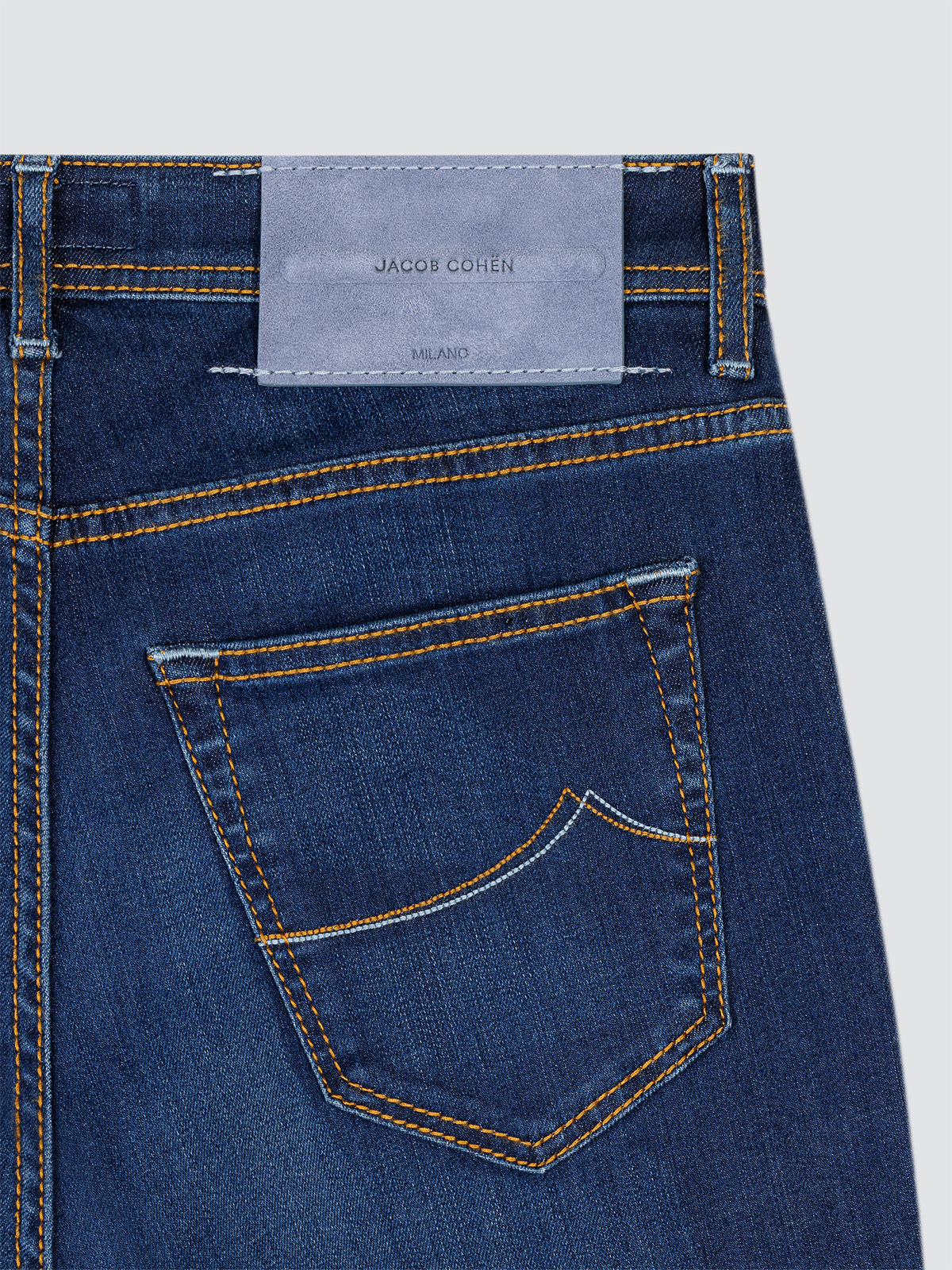 Close-up of blue jeans with a Jacob Cohen label on a light gray background