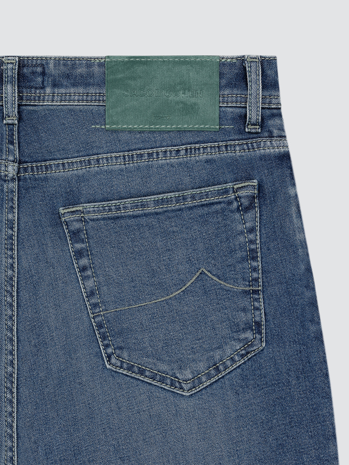 Close-up of blue denim jeans with a green patch on a light gray background