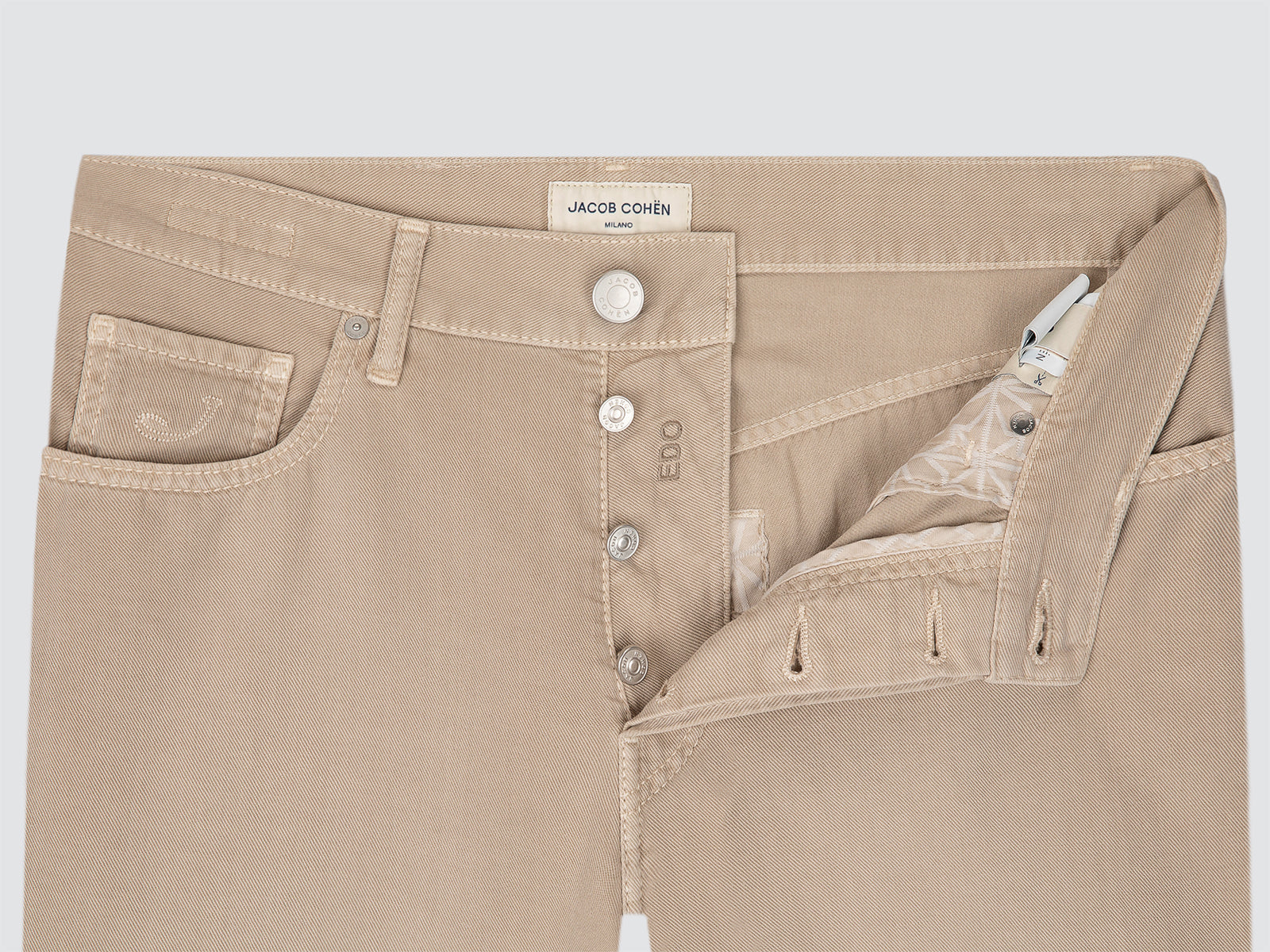 Close-up of beige pants with a brand label on a light gray background