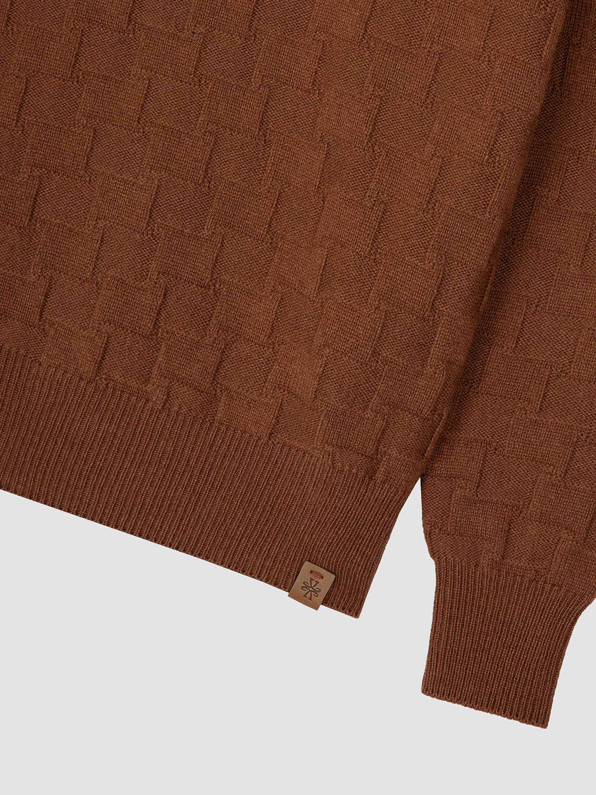 Close-up of a textured brown knit sweater showing the ribbed hem and sleeve cuff with a small fabric brand tag.