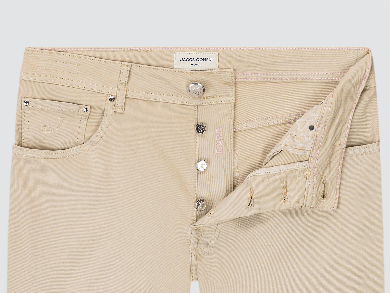 Beige pants with a close-up of the waistband and buttons on a light gray background.