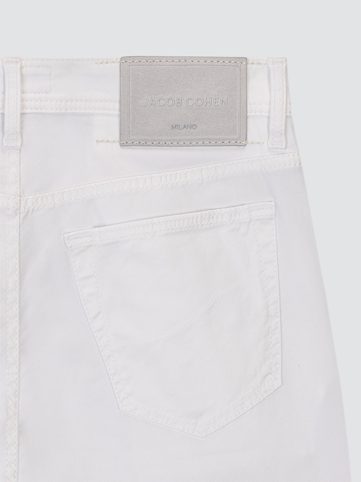 Close-up of a white gabardine 5 pockets with a brand label Jacob Cohen on a light gray background
